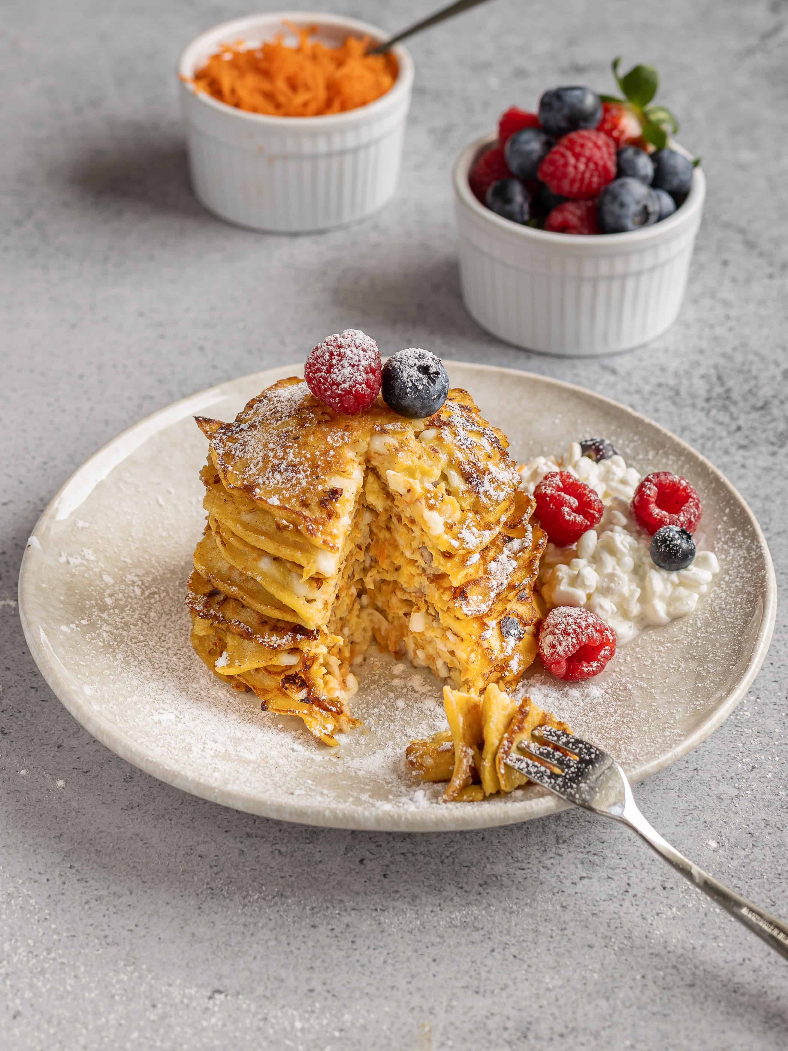 Pannkakor med bär, grädde och pudrat socker på en tallrik.