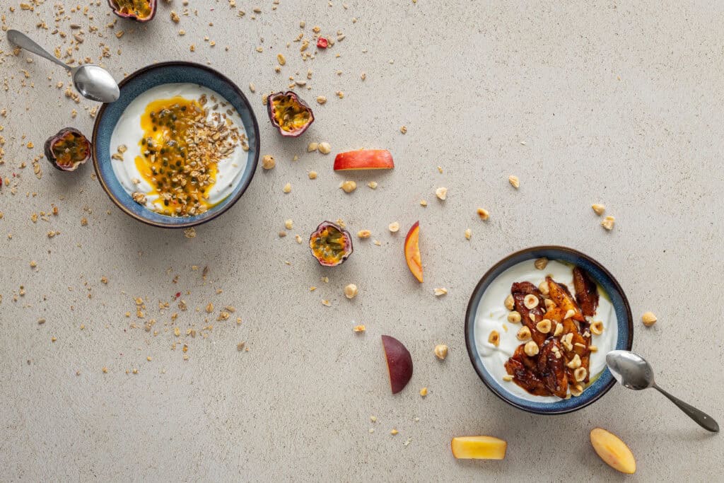 Läckra dessertskålar med passionsfrukt, nötter och frukt på en ljus bakgrund.