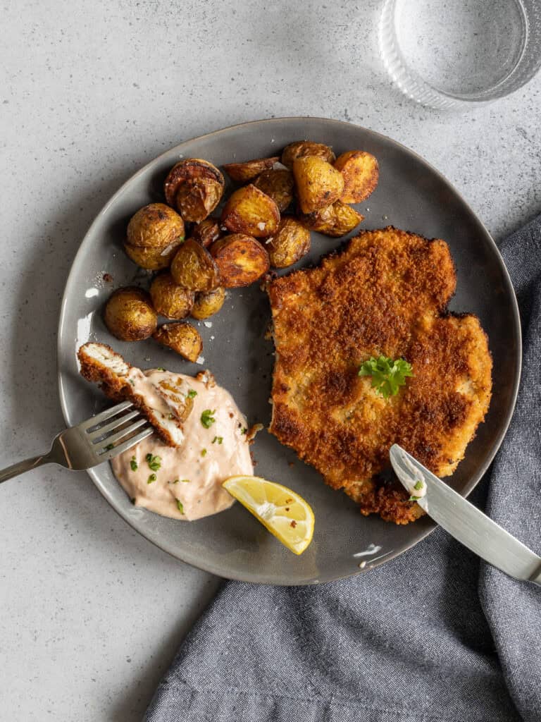 Fisk- och potatisrätt med krispig panering, potatis och sås på en tallrik.