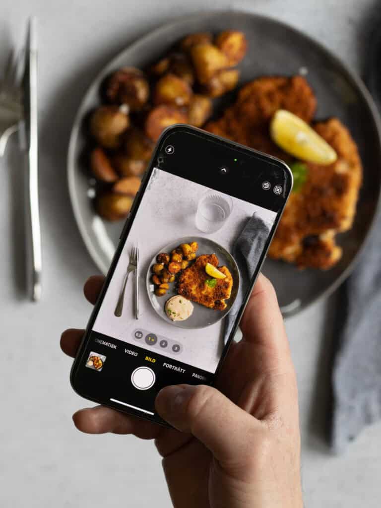 Person som tar bild av mat på tallrik med smartphone i hand.