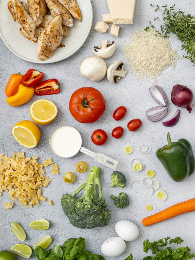 Bild av färska grönsaker och kycklingfilé på ett köksbord för matlagning.