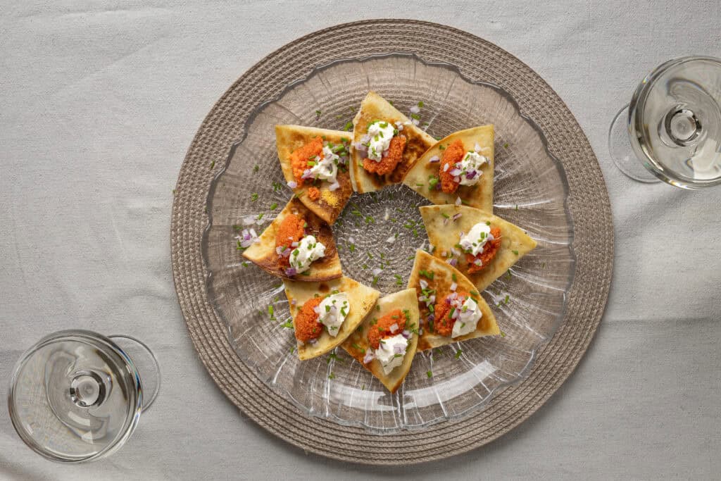 Små aptitretare med ost och blommor på ett glasfat.