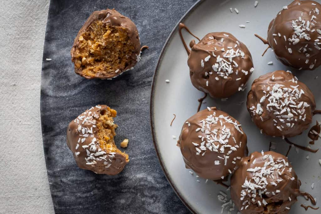 Färska chokladbollar med kokos på en tallrik, några är delvis uppätna.
