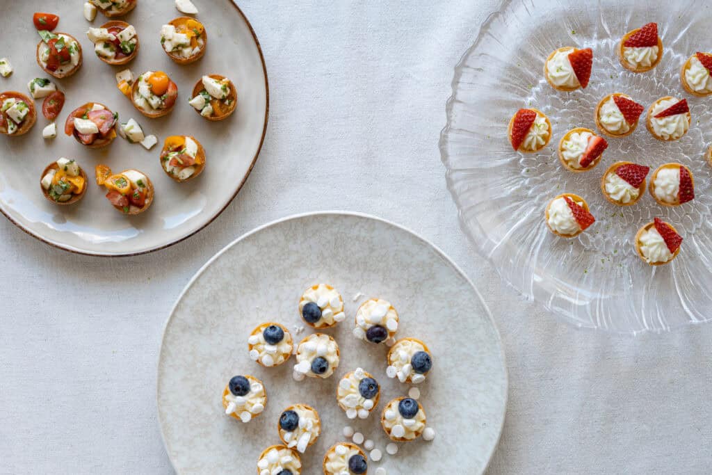 Läckra små desserter på tre olika fat, dekorerade med frukt och bär, perfekt för fest eller tilltugg.