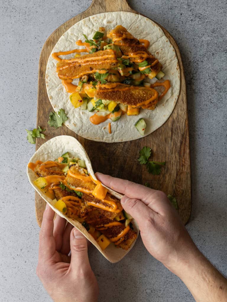 Vegetariska tacos med fisk, grönsaker och salsa på en träskärbräda.