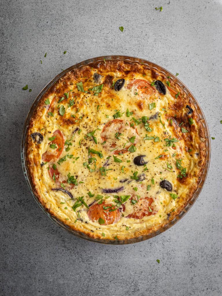 Vegetarisk pizza med tomater, paprika, lök och oliver på en grå bakgrund.