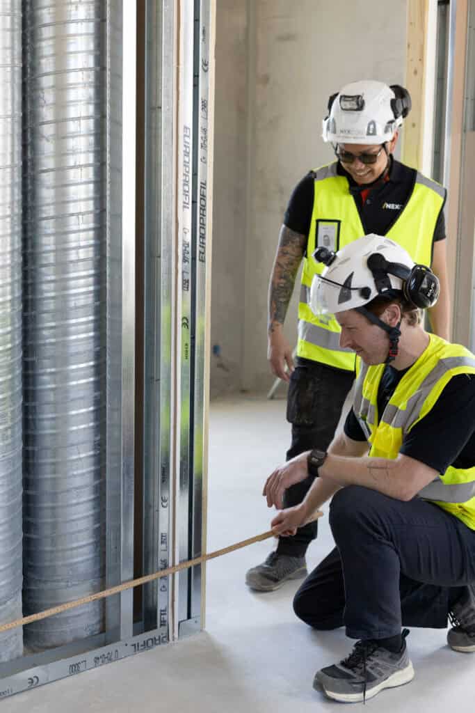 Säkerhetsutrustade byggarbetare inspekterar installation i ett nybyggt utrymme.