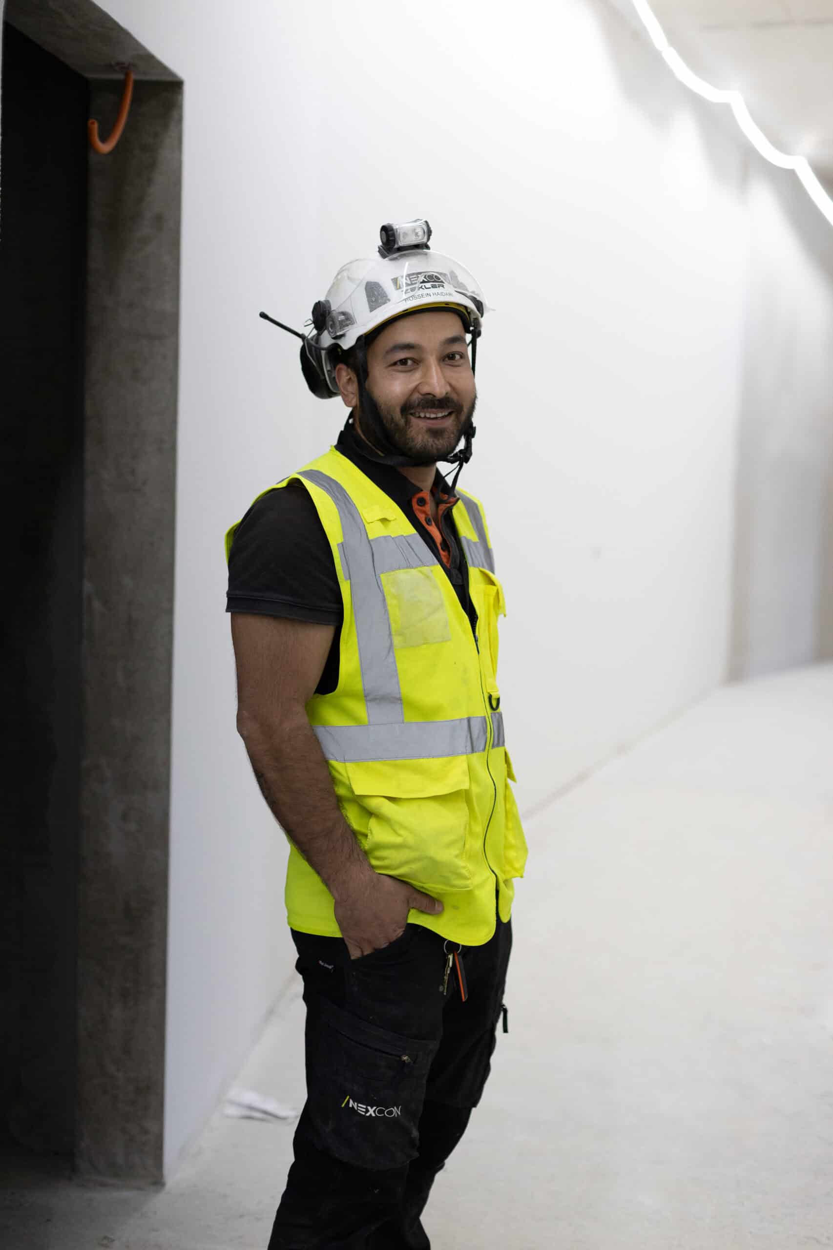 Byggarbetare i skyddsutrustning, leende, i en modern inomhusmiljö.