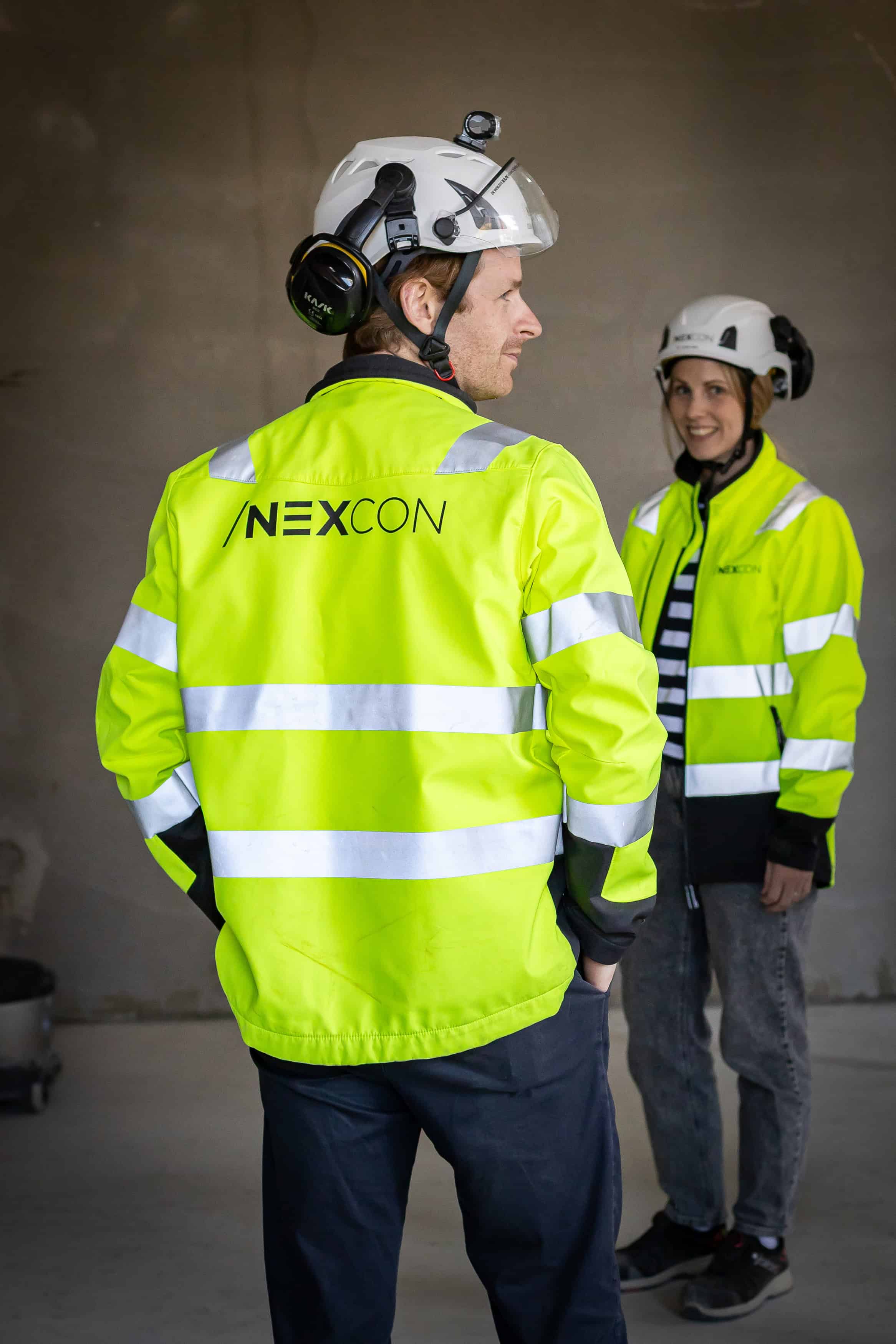 Byggarbetare i höga synliga kläder och hjälmar, samtalar i en industriell miljö.