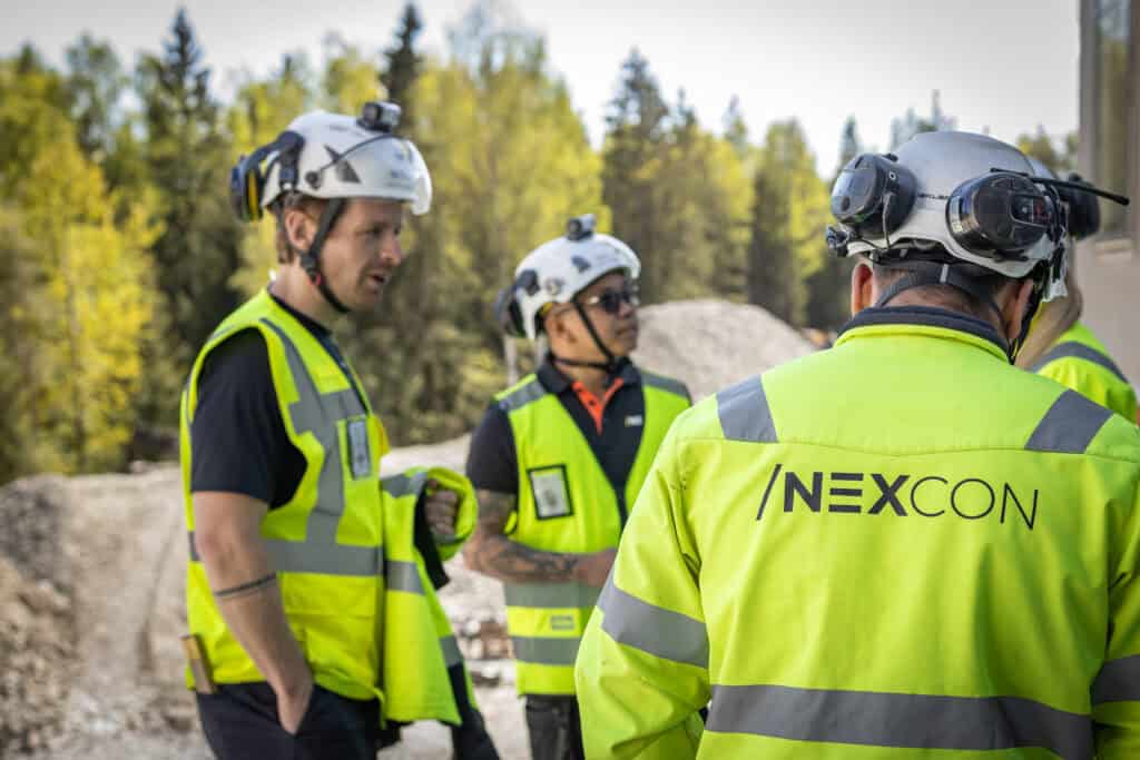 Byggarbetare i höga synliga västar och hjälmar diskuterar på byggplatsen.