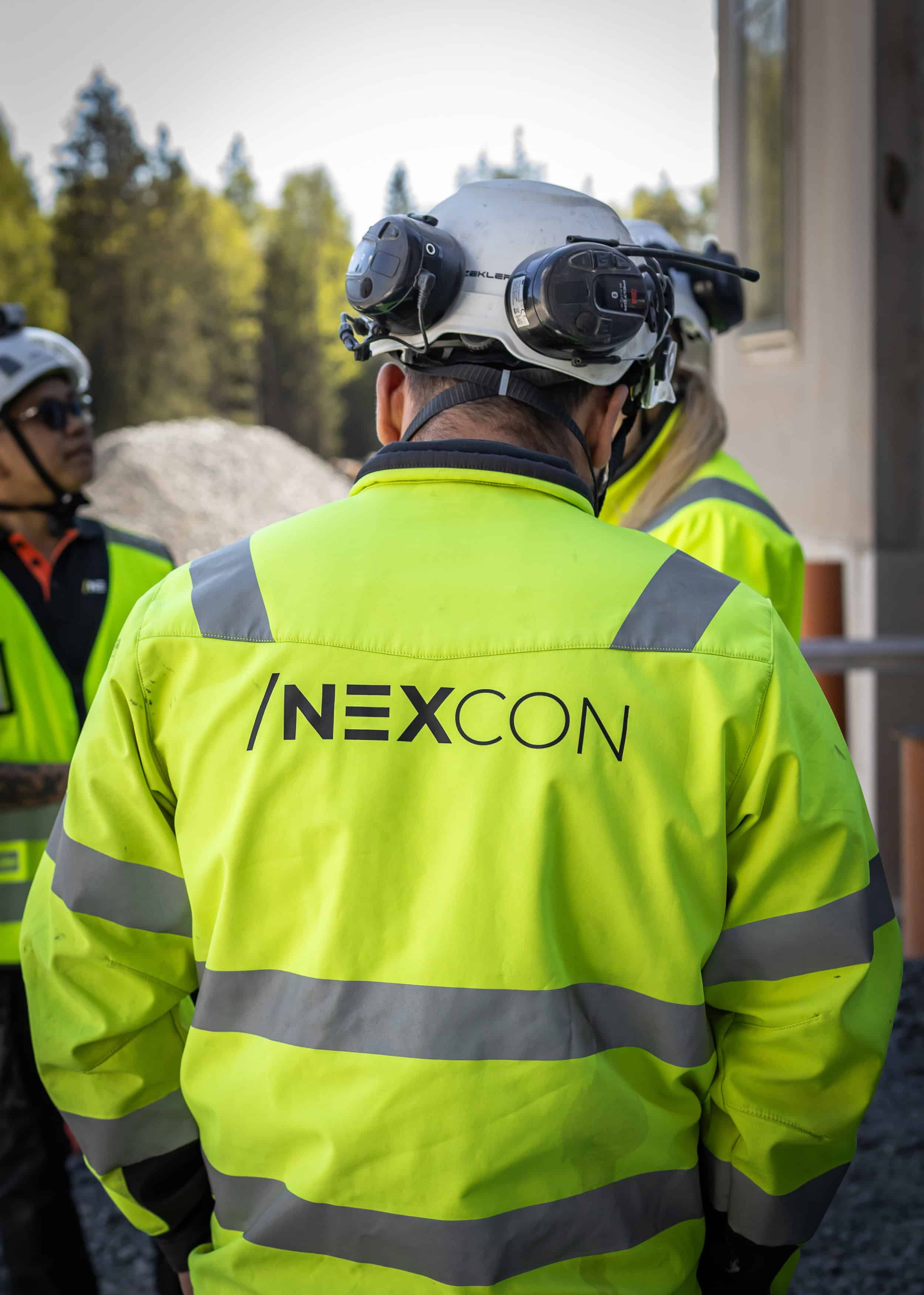 Byggarbetare i högsynkig väst med NEXCON-logga, utomhus i byggmiljö.