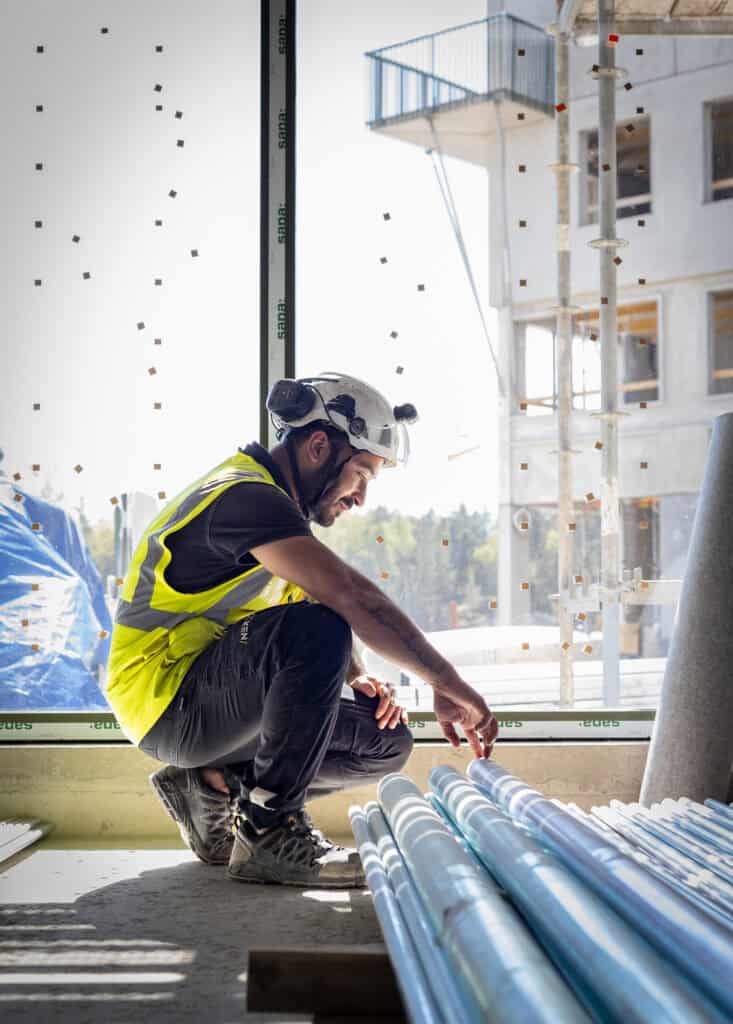 Byggarbetare i säkerhetsutrustning inspekterar rör på byggplats i Uppsala.