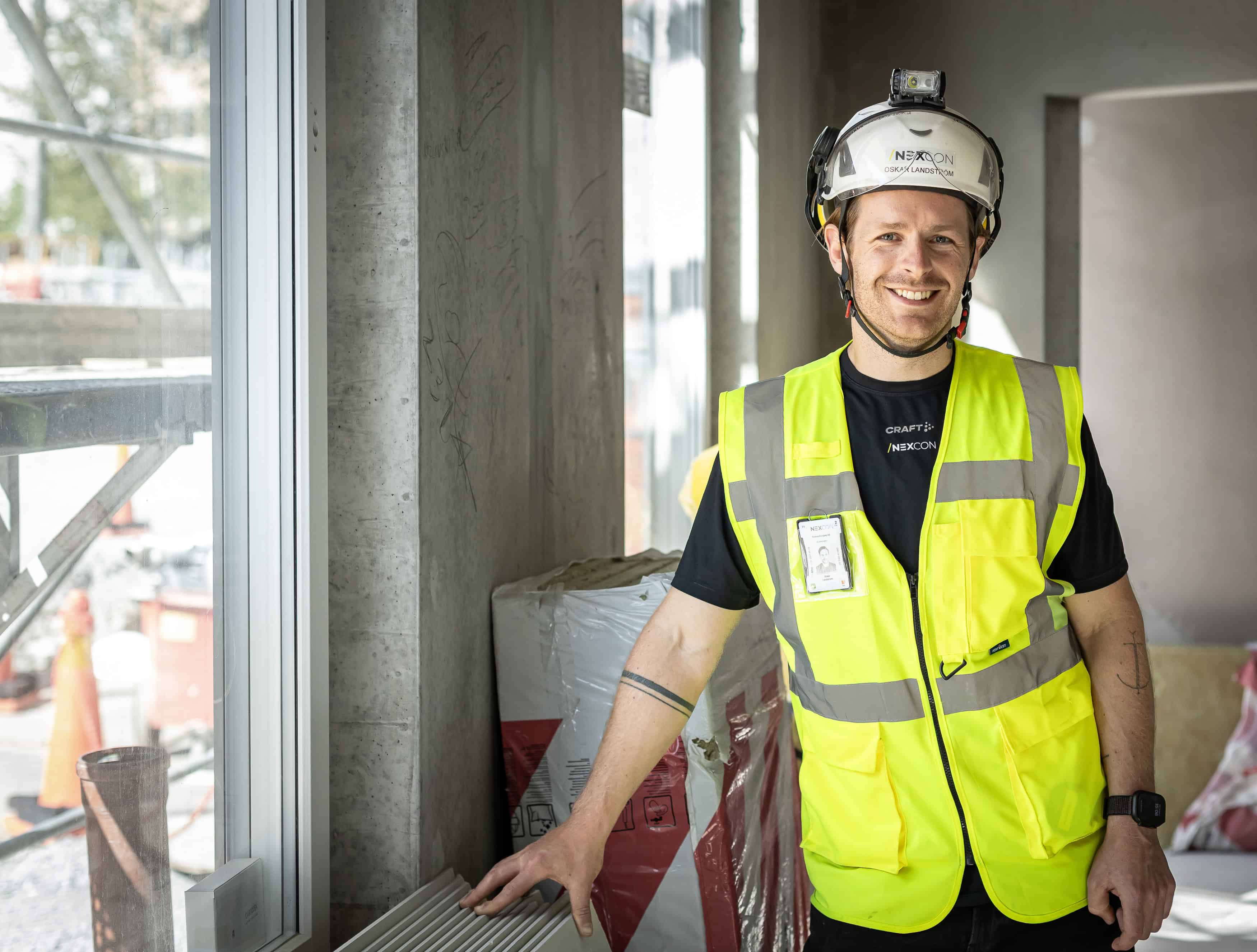 Byggarbetare i inomhusmiljö, leende, i hög synlighet väst.