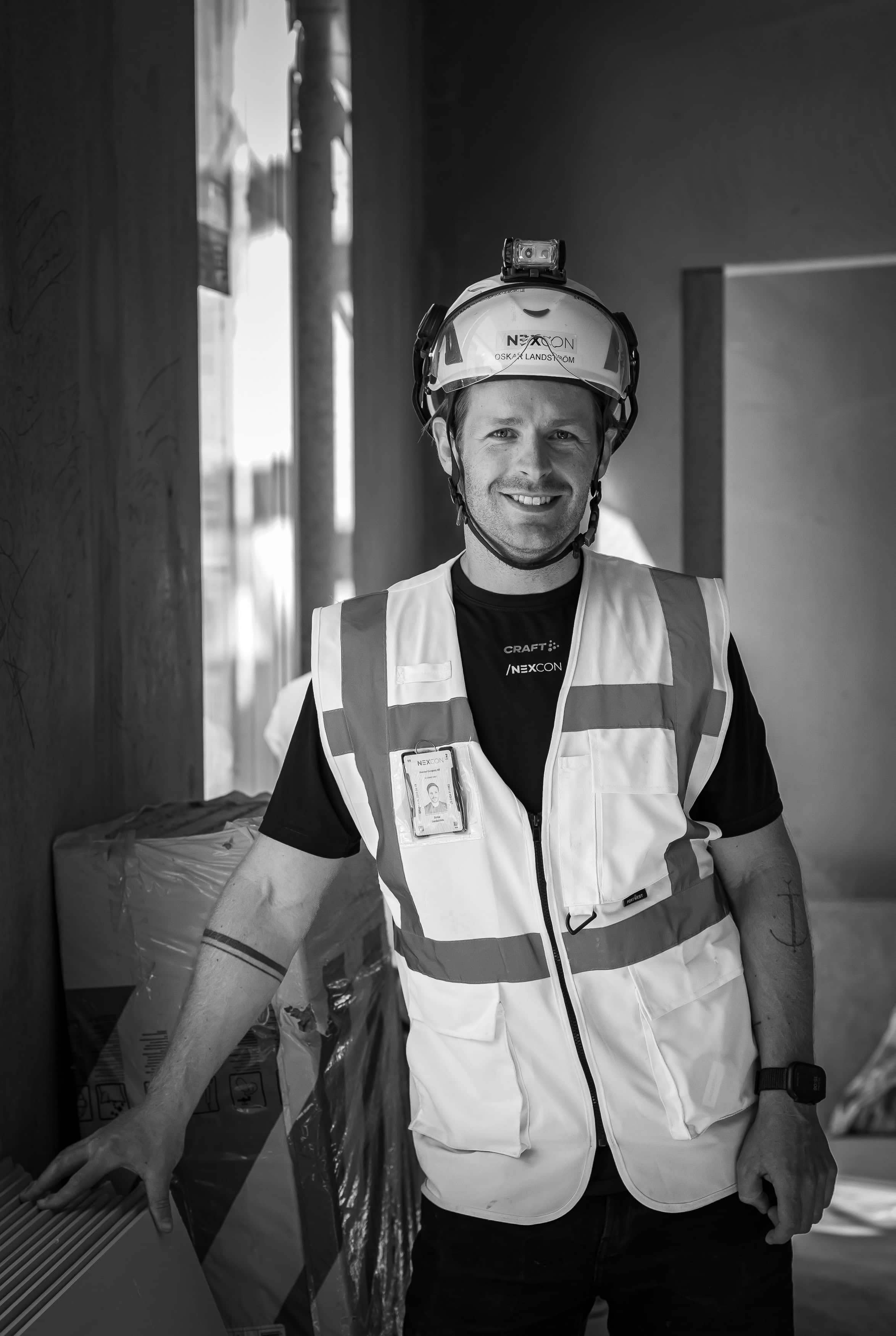 Byggarbetare i säkerhetsutrustning, leende, inomhus, professionell foto.