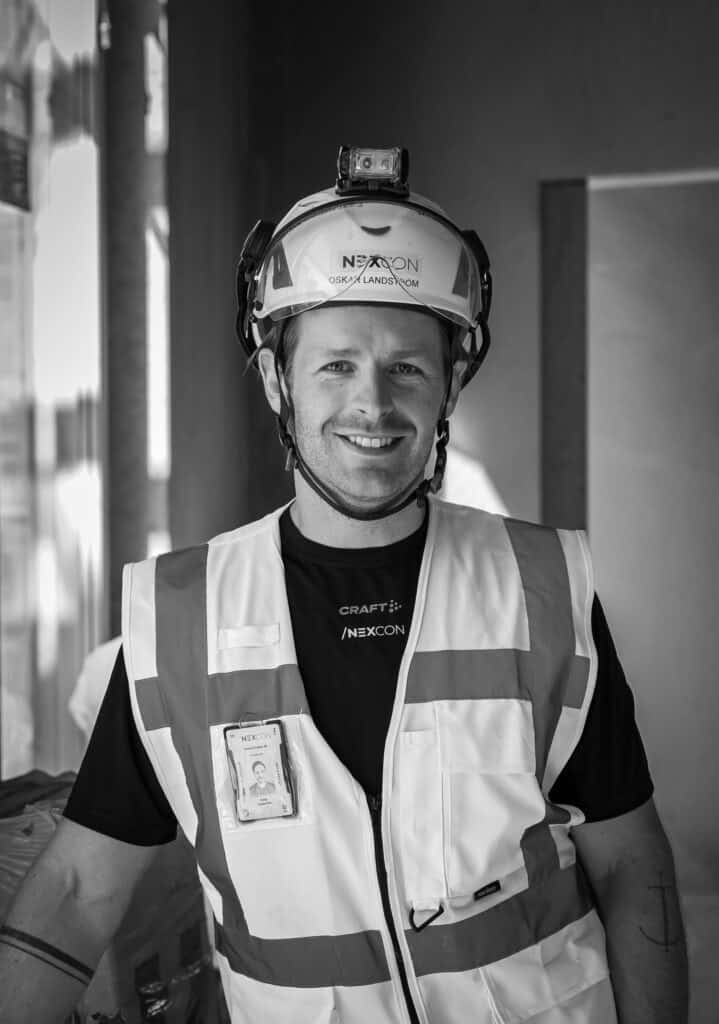 Byggarbetare i säkerhetsutrustning med hjälm och väst, leende inomhus.