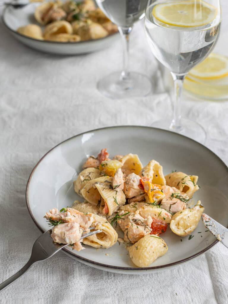 Räkrätt med pasta och dill på vit tallrik, drycker i bakgrunden.