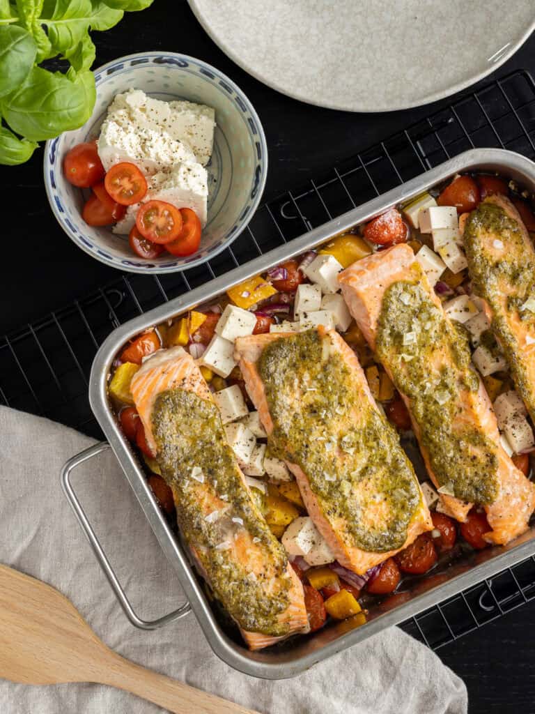 Ugnsbakad laxfilé med pestotäcke på en bädd av färska grönsaker och tomater.