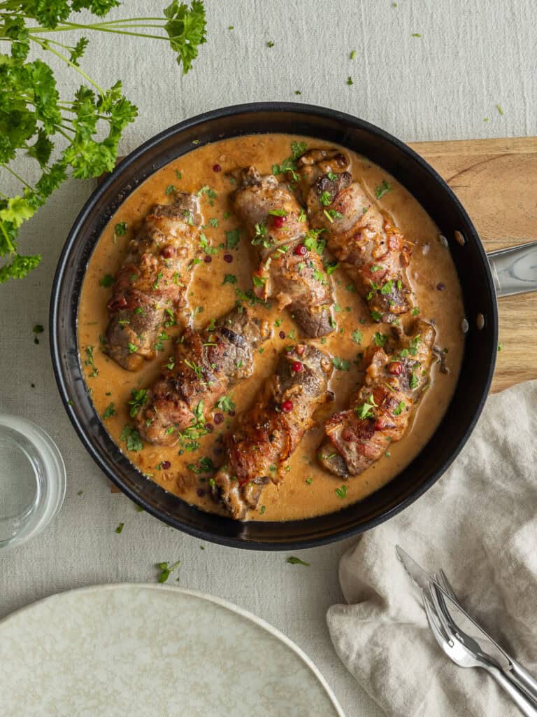 Köttbullar i krämig gräddsås med örter och kryddor. Serveras i en svart panna på ett rustikt bord.