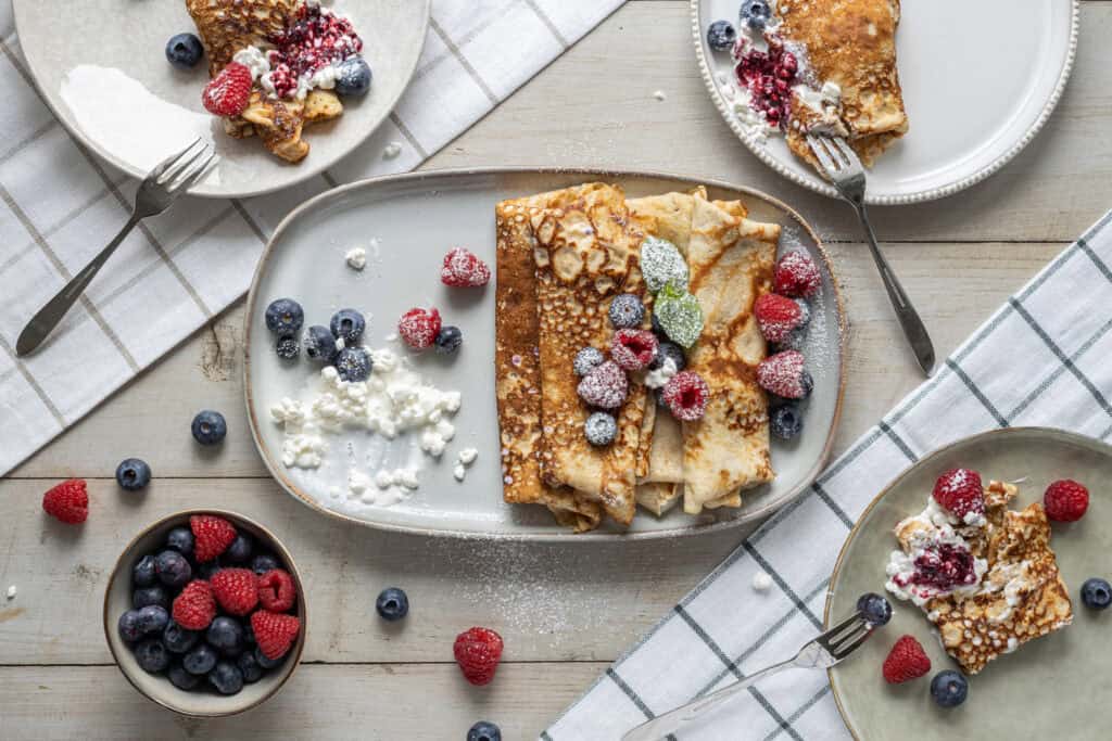 Bärpannkaka med färska blåbär, hallon och jordgubbar på en vit tallrik.